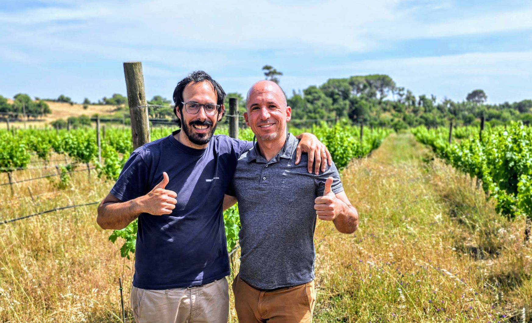 Two smiling winemakers giving thumbs up in a Portuguese vineyard